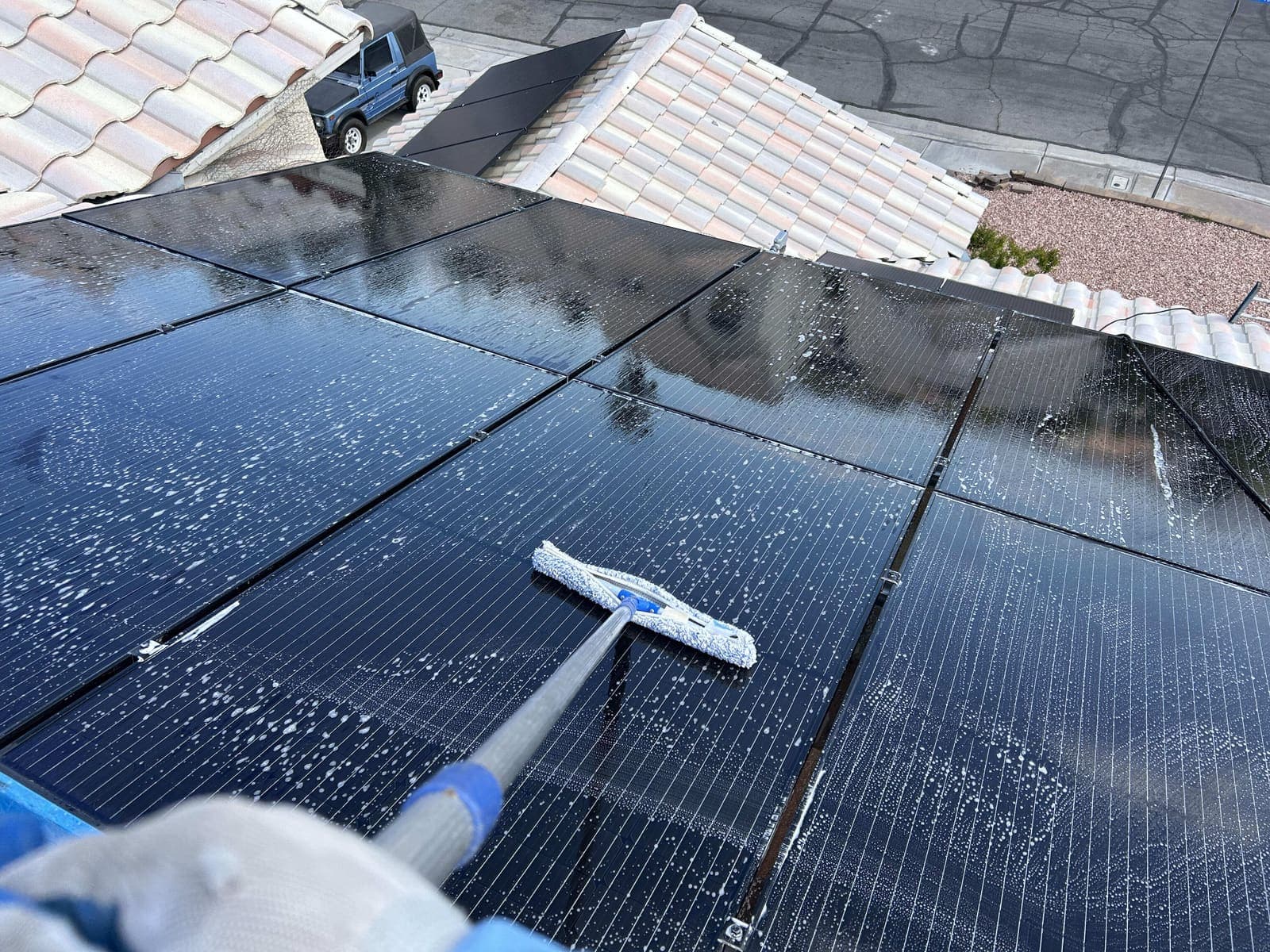 Technician squeegeeing a solar panel with a house in the background